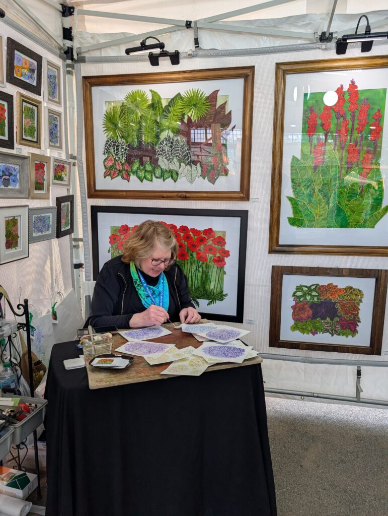 Artist at 4 Bridges Art Festival sitting down working at her booth.