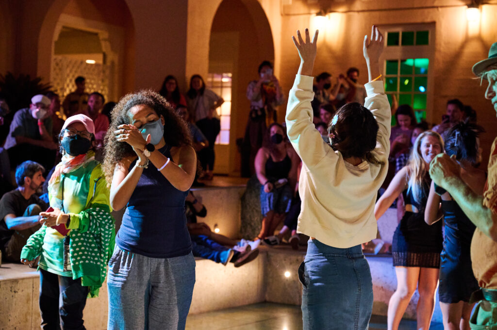 A bunch of young adults with masks dancing inside a building.