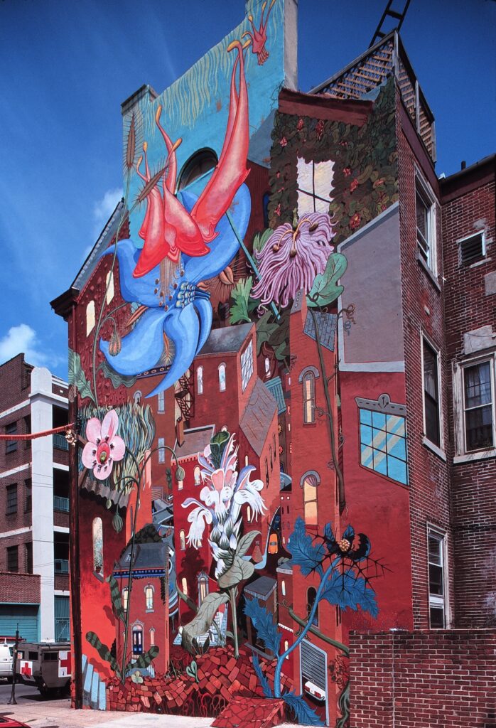 A colorful mural on a brick building depicting large flowers and abstract buildings against a blue sky.